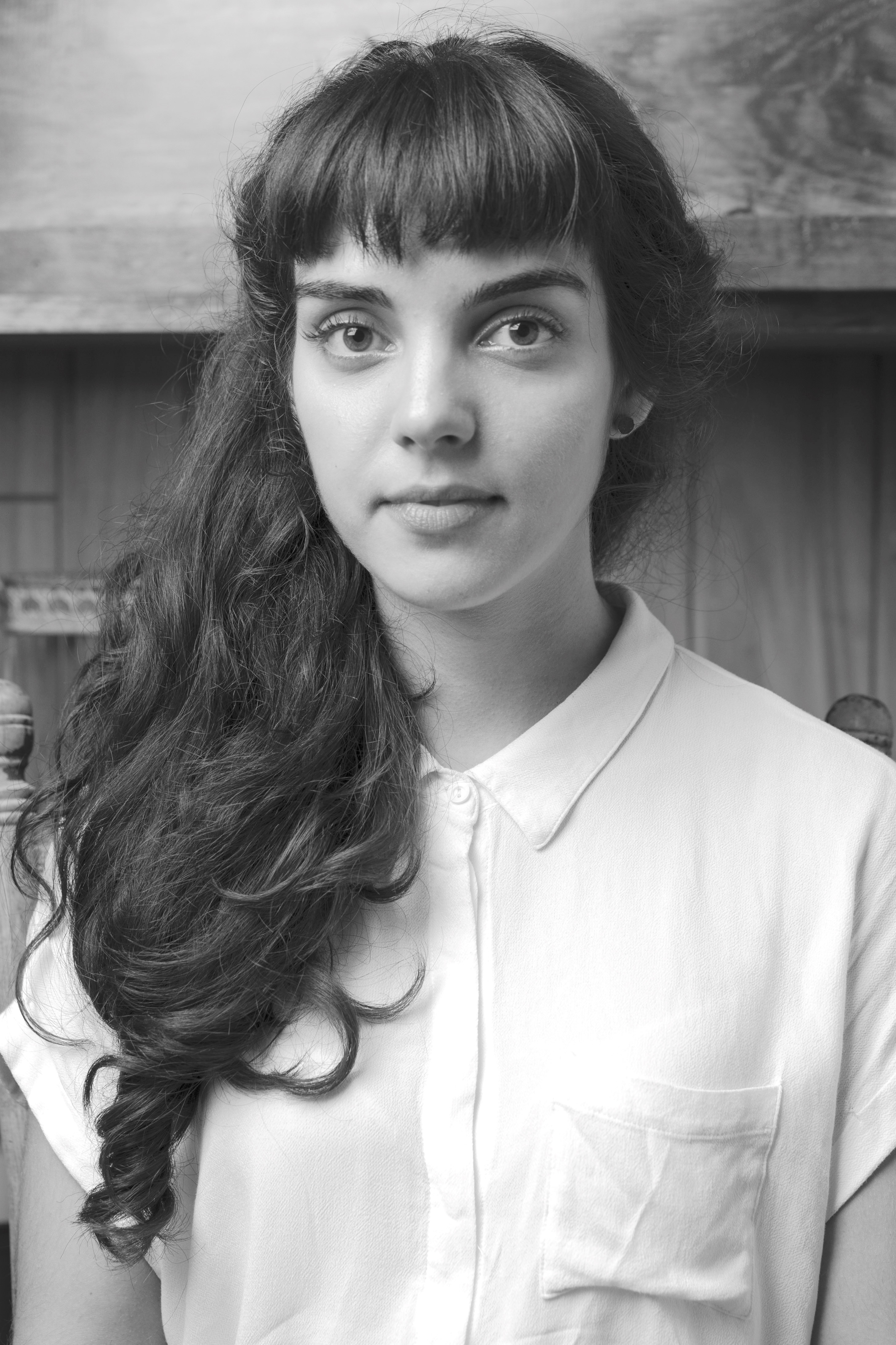 Portrait of the author, featuring unruly, dark hair and blunt bangs, two eyes, a nose, and a mouth, as well as a dangerously white collared shirt.